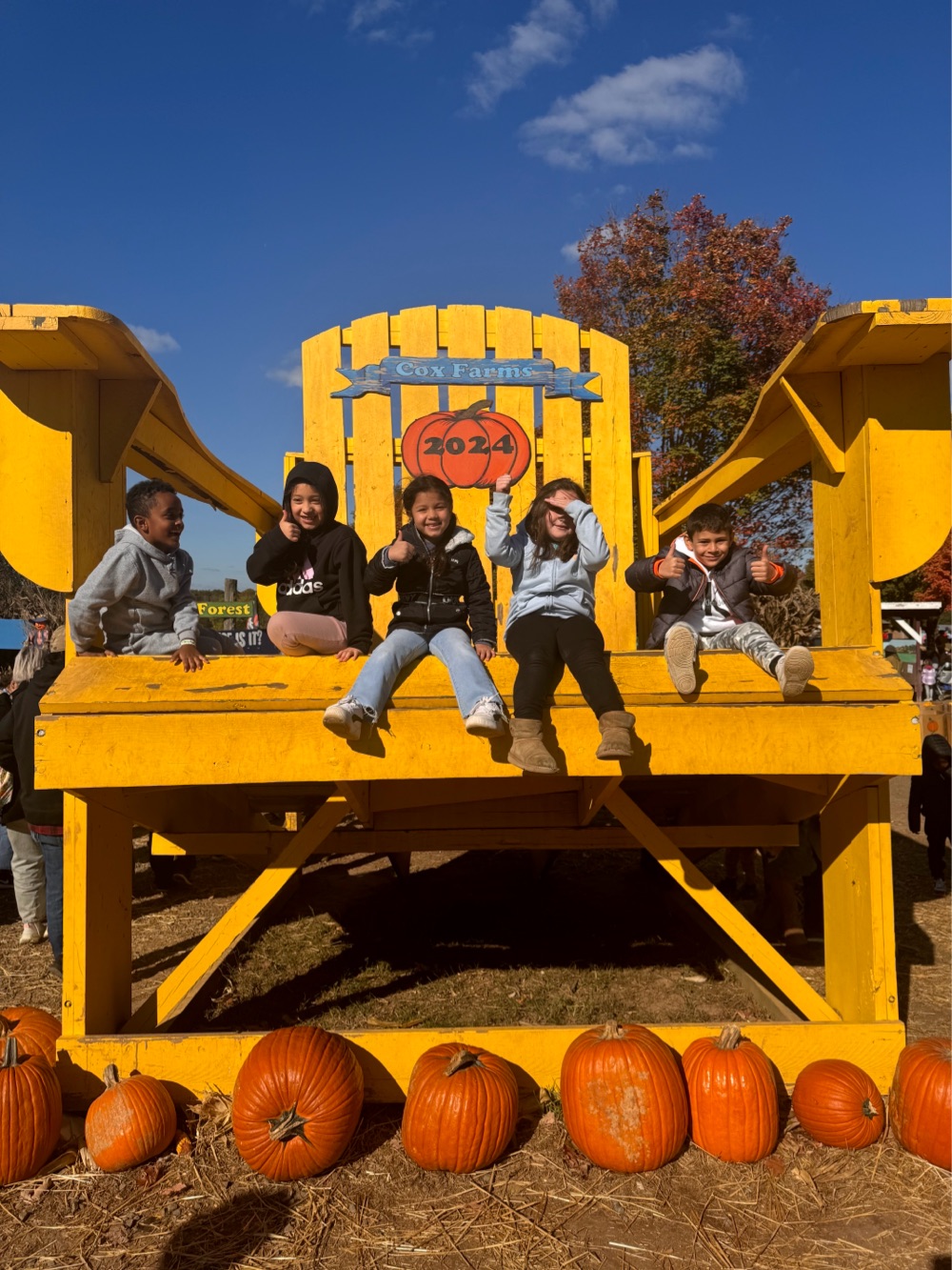 Students pose on giant adarondack chair during 1st grade field trip